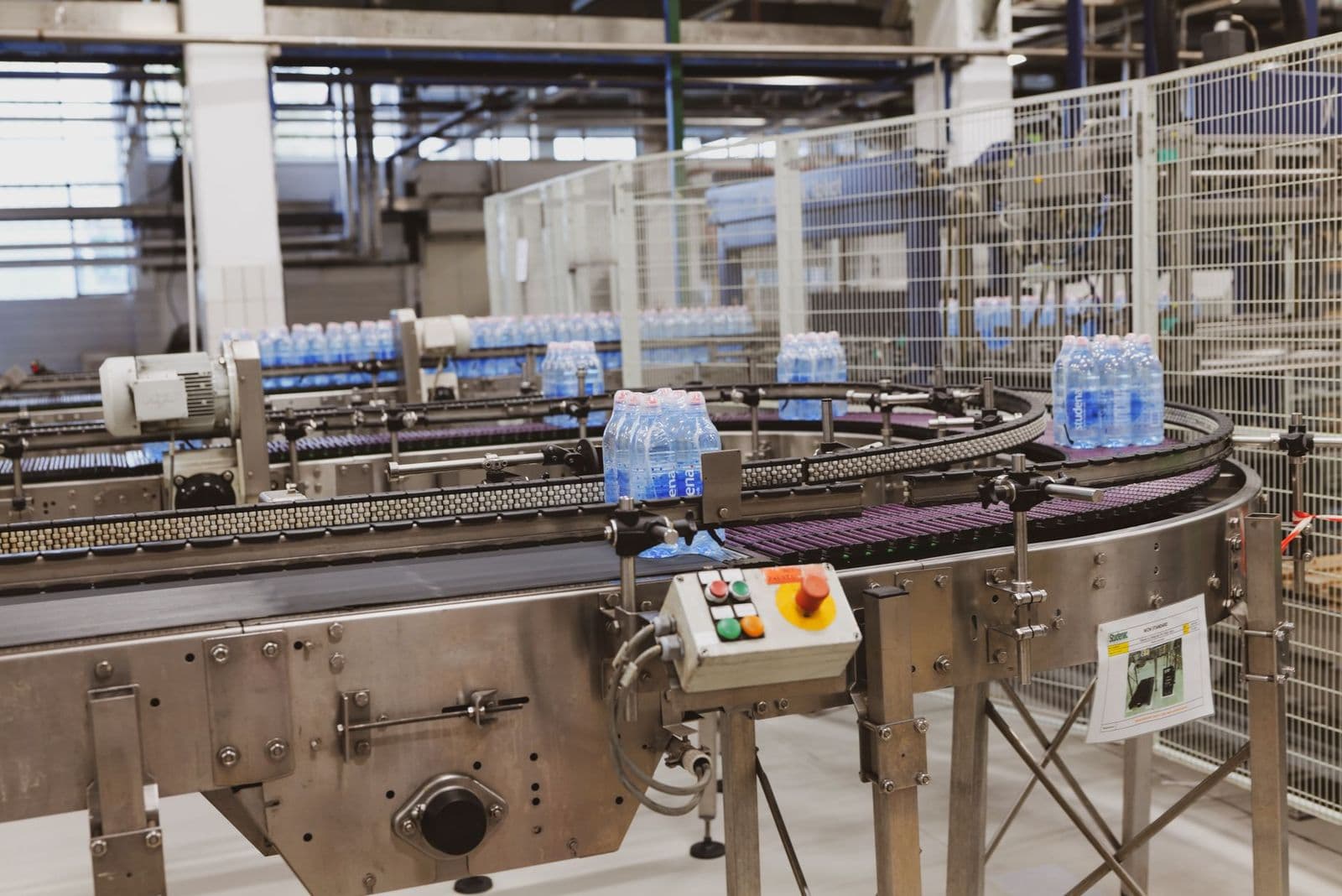 Bread rolls moving along a stainless-steel conveyor belt in a food factory, inspected under bright industrial lighting